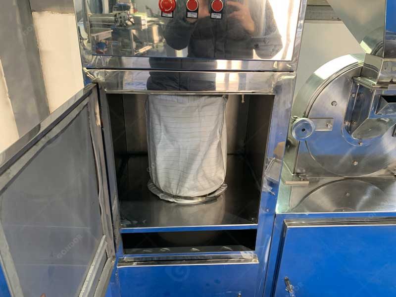 Fabric collection bag inside the lower cabinet of a cocoa powder grinder