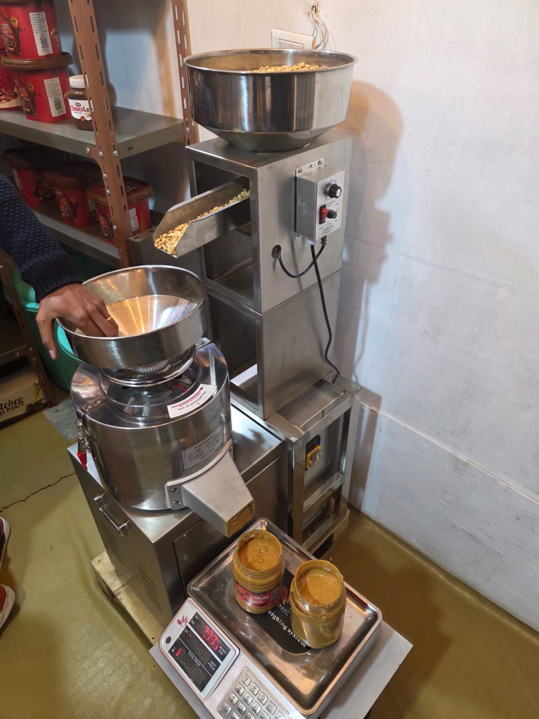 Automatic feeder metering roasted peanuts into a colloid mill producing peanut butter in a shop