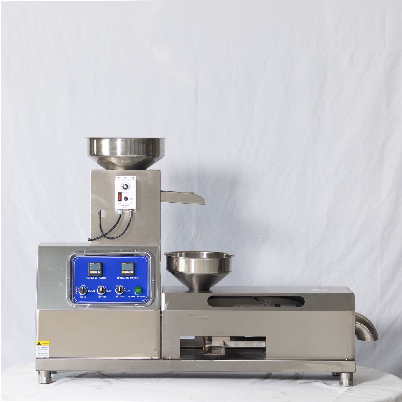 Automatic press feeder fitted above a small screw oil press with English-labelled control panel